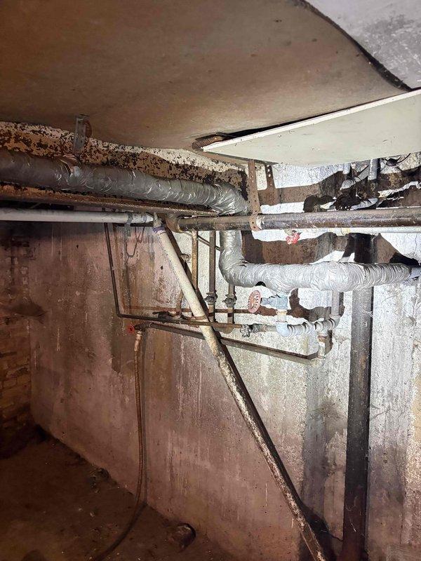 Conducted plumbing estimate for extensive pipe replacement in basement area. Documented severely corroded metal piping throughout crawl space with heavy rust buildup and structural deterioration, along with aged HVAC ductwork and deteriorated insulation. Assessed moisture-damaged concrete block walls showing mineral deposits and water staining, evaluated multiple pipe runs requiring replacement due to advanced corrosion, and photographed existing conditions for comprehensive piping system replacement proposal.