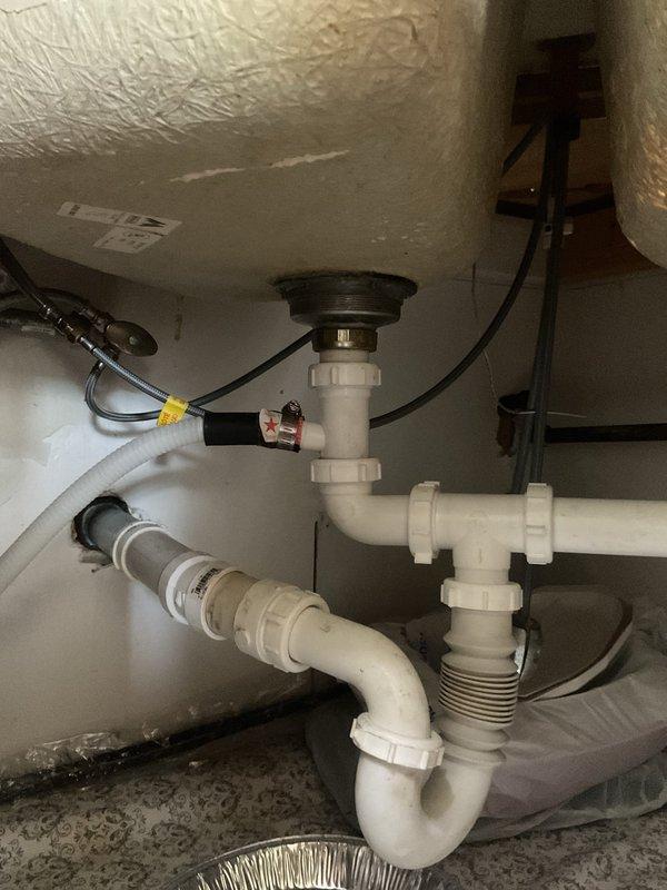 Responded to service call for multiple drainage issues including clogged bathtub, leaking kitchen sink, and frequently clogging toilet. Inspected kitchen sink plumbing beneath cabinet, examining P-trap drainage system, PVC connections, and slip joints for signs of leakage or blockage. Assessed bathtub corner installation with three-valve fixture system, noting drain and overflow assemblies requiring attention. Performed diagnostic evaluation of all affected fixtures to identify root causes of recurring drainage problems and water leakage at kitchen sink connection points.