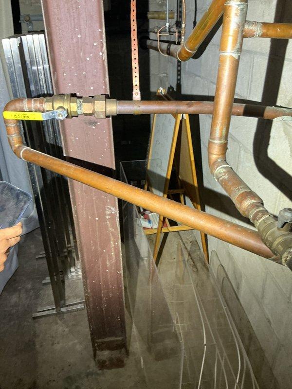 Conducted comprehensive assessment of water main service infrastructure for commercial property requiring system upgradation. Evaluated existing copper piping network in mechanical room, documenting current condition of horizontal and vertical runs with insulation showing age-related deterioration. Identified standing water accumulation on mechanical room floor, indicating potential drainage concerns or active leak requiring immediate attention during upgrade process. 

Assessed exterior water service entry point and street-side infrastructure including fire hydrant placement and connection points within pedestrian plaza area. Documented brick paver surface conditions and accessibility requirements for excavation and main line replacement work. Photographed existing service routing from street connection through building foundation to interior distribution system. Prepared technical documentation and photographic evidence to support water main upgrade specifications, including pipe siz