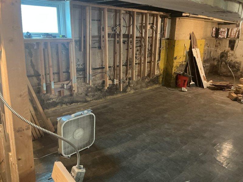 Conducted comprehensive assessment of unfinished basement for drain tile system installation and rough plumbing estimate. Inspected existing ejector pit system and evaluated extensive water intrusion damage evidenced by significant mold growth and dark staining along lower wall framing and concrete foundation. Assessed current plumbing configuration including partially installed toilet fixture, vertical PVC ventilation stack, and copper supply lines. Documented basement conditions showing active moisture issues requiring remediation, evaluated structural framing and concrete floor for drain tile installation feasibility, and photographed all relevant areas to prepare detailed estimate for interior perimeter drain tile system, ejector pit evaluation/replacement, and complete rough plumbing installation for bathroom fixtures.