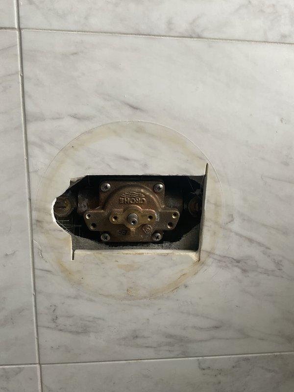 Responded to service call for non-functional shower in primary bathroom. Upon inspection, found shower valve assembly requiring replacement due to internal component failure. Removed existing brass diverter valve and mixing mechanism from recessed wall cavity in marble-patterned tile surround. Assessed water damage and staining around valve opening, confirming source of operational failure. Documented existing plumbing configuration including tub spout with diverter and drain assembly for replacement valve specifications and estimate preparation.