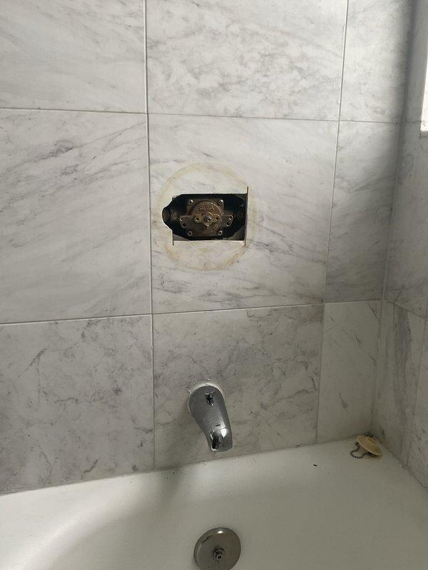 Responded to service call for non-functional shower in primary bathroom. Upon inspection, found shower valve assembly requiring replacement due to internal component failure. Removed existing brass diverter valve and mixing mechanism from recessed wall cavity in marble-patterned tile surround. Assessed water damage and staining around valve opening, confirming source of operational failure. Documented existing plumbing configuration including tub spout with diverter and drain assembly for replacement valve specifications and estimate preparation.