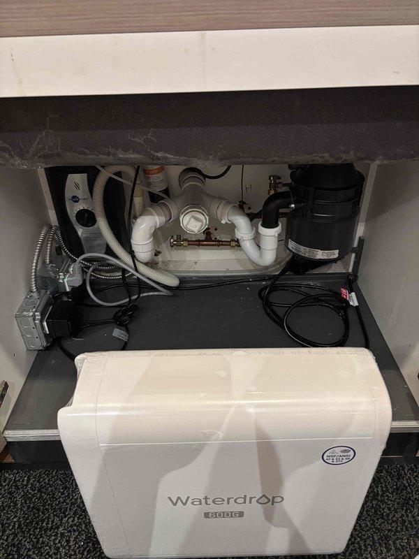 Installed Waterdrop Studio water filtration system beneath kitchen sink, connecting unit to existing plumbing infrastructure including supply lines, drain assembly, and garbage disposal. Completed installation with proper integration to PVC drain pipes, supply connections, and verified system operation with leak testing.