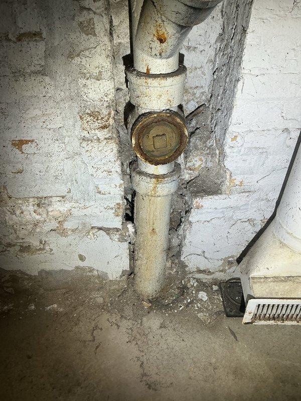 Performed sewer scope inspection of underground drainage system to assess pipe condition and identify potential issues. Inspection revealed aging plumbing infrastructure in basement area, including deteriorated sump pit with mineral deposits and corroded piping systems with significant rust staining and paint deterioration on surrounding surfaces. Documented findings with photographic evidence showing sump pump basin condition, main shutoff valve assembly, and overall state of basement plumbing components for estimate preparation.