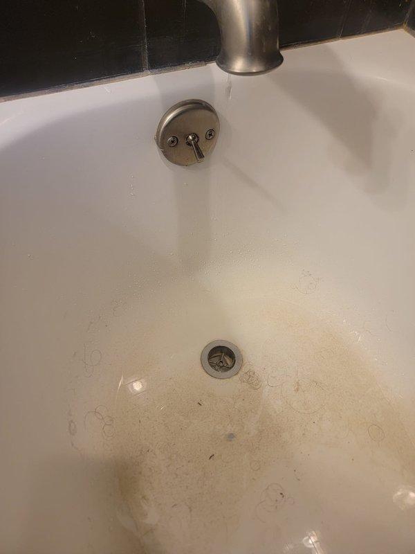 Responded to service call for clogged bathtub and sink. Upon inspection, found significant buildup of hair, debris, and mineral deposits around drain assemblies in both fixtures. Bathroom sink exhibited water staining and sediment accumulation around the chrome drain and overflow plate. Bathtub drain connection showed deteriorated flexible hose with extensive grime, soap scum, and fiber debris tangled around the white plastic fitting. Cleared obstructions from both drain lines, removed accumulated debris, and restored proper drainage function to both fixtures.