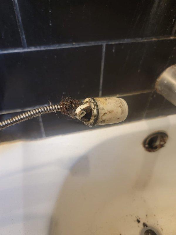 Responded to service call for clogged bathtub and sink. Upon inspection, found significant buildup of hair, debris, and mineral deposits around drain assemblies in both fixtures. Bathroom sink exhibited water staining and sediment accumulation around the chrome drain and overflow plate. Bathtub drain connection showed deteriorated flexible hose with extensive grime, soap scum, and fiber debris tangled around the white plastic fitting. Cleared obstructions from both drain lines, removed accumulated debris, and restored proper drainage function to both fixtures.