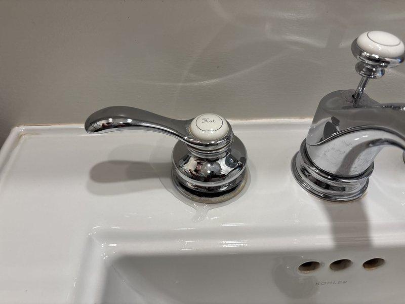Responded to a leaky bathroom sink faucet complaint and performed a thorough inspection of the Kohler sink assembly and chrome three-piece faucet fixture. Upon examination, identified the source of the leak and addressed the issue by servicing the valve assemblies and faucet handles. Documented the existing installation with photographs showing the hot and cold water handles, central spout, and overall fixture condition prior to completing repairs.