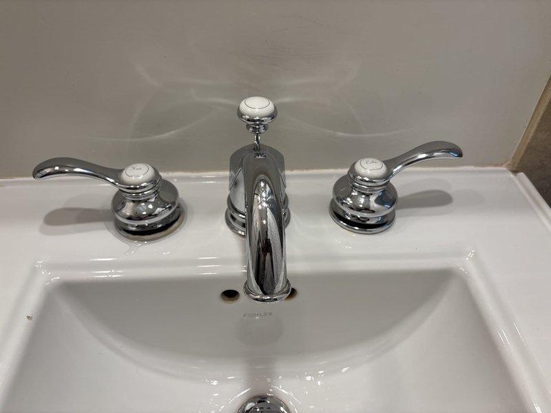 Responded to a leaky bathroom sink faucet complaint and performed a thorough inspection of the Kohler sink assembly and chrome three-piece faucet fixture. Upon examination, identified the source of the leak and addressed the issue by servicing the valve assemblies and faucet handles. Documented the existing installation with photographs showing the hot and cold water handles, central spout, and overall fixture condition prior to completing repairs.