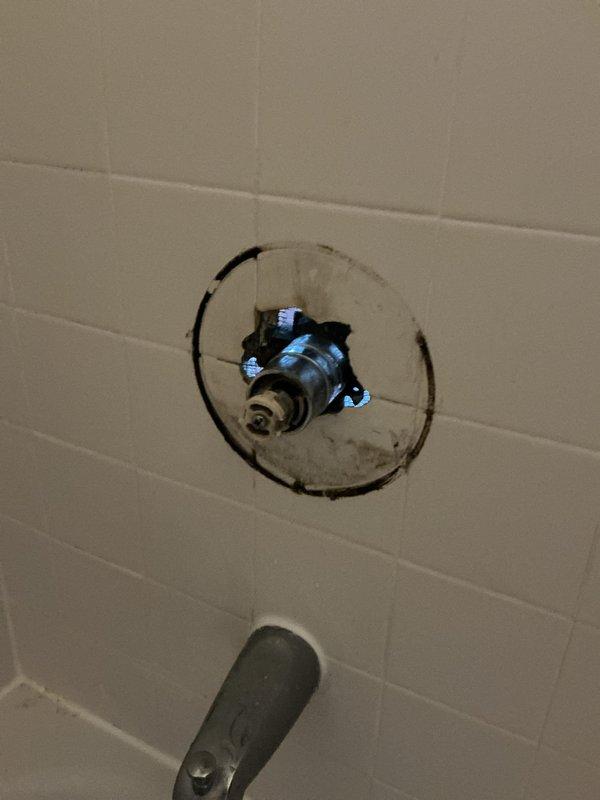 Responded to service call for shower valve issues. Upon inspection, found the shower stopper mechanism was loose and the valve handle trim piece had broken off, preventing proper operation of the fixture. Accessed the plumbing through existing wall access panel, exposing aged copper supply lines with visible oxidation and foam pipe insulation. Documented the condition of the valve assembly behind the white subway tile wall, noting the valve stem and internal components requiring attention. Photographed the exposed plumbing infrastructure and damaged valve hardware for estimate preparation and customer review.