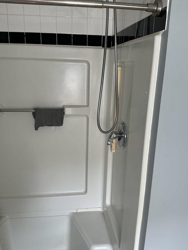Conducted site assessment for upcoming top floor bathroom renovation. Documented existing conditions including white fiberglass shower enclosure with built-in shelving, chrome handheld showerhead assembly, and decorative tile work featuring black accent border. Photographed complete bathroom layout including vanity, toilet, and shower/tub unit to establish baseline for remodel planning. Noted basement pipe concern for follow-up evaluation during scheduled renovation appointment.