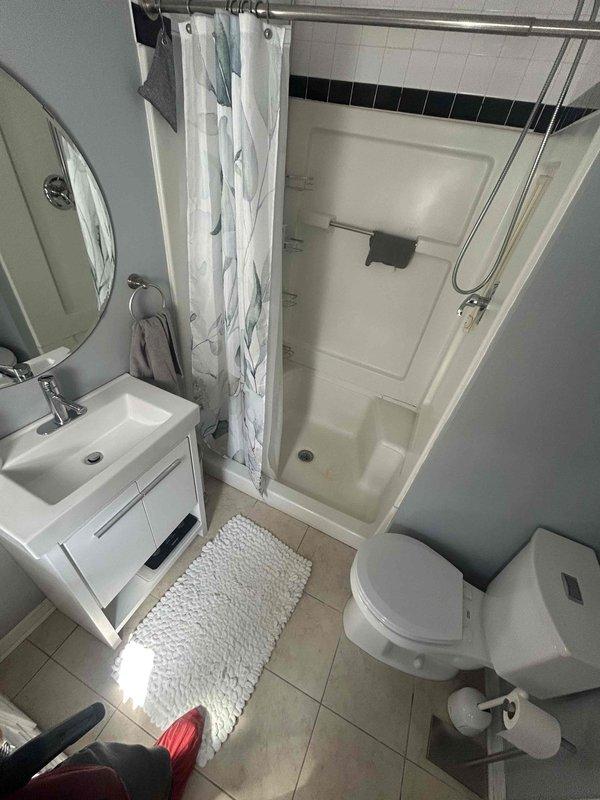 Conducted site assessment for upcoming top floor bathroom renovation. Documented existing conditions including white fiberglass shower enclosure with built-in shelving, chrome handheld showerhead assembly, and decorative tile work featuring black accent border. Photographed complete bathroom layout including vanity, toilet, and shower/tub unit to establish baseline for remodel planning. Noted basement pipe concern for follow-up evaluation during scheduled renovation appointment.