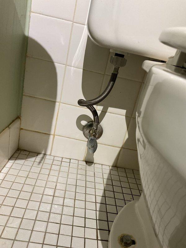 Responded to active water leak at toilet tank supply connection. Upon arrival, inspected the flexible stainless steel braided supply line and wall-mounted chrome shut-off valve. Identified leak at connection point between supply line and toilet tank fill valve. Shut off water supply at wall valve and posted notification signage to prevent toilet use during repair. Disconnected faulty supply line connection, inspected tank threads and inlet valve for damage or corrosion. Cleaned connection surfaces, replaced worn rubber washer, and reinstalled supply line with proper hand-tightening followed by wrench adjustment to manufacturer specifications. Restored water supply and tested connection under full pressure for leaks. Verified proper fill valve operation and tank refill cycle. Inspected surrounding floor tiles and wall area for water damage; noted pre-existing age-related discoloration but no new moisture damage from leak. Removed signage and returned toilet to service with no active lea