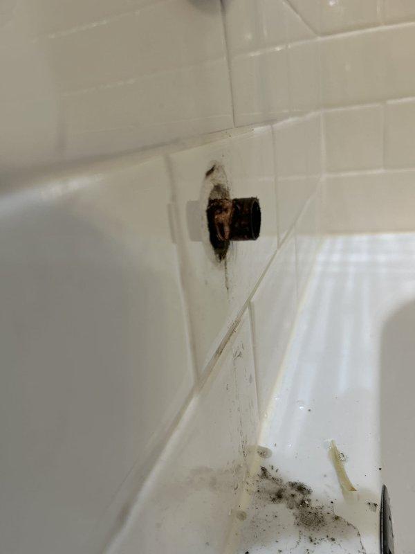 Responded to water leak complaint from downstairs unit reporting ceiling water intrusion originating from master bathroom area. Upon inspection, identified corroded and deteriorating tub drain assembly with visible rust, water staining, and compromised seals at the fixture-to-tile interface. Evidence of chronic moisture penetration was observed in surrounding grout lines and tile corners, with active dampness detected on subfloor beneath bathtub access panel. The leak was triggered by draining bathwater, indicating failed drain gasket or compromised plumbing connection allowing water to bypass the drain system and seep through the floor assembly to the unit below.