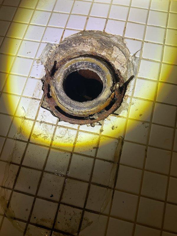 Responded to report of leak at base of toilet in commercial restroom facility. Upon inspection, discovered severely deteriorated floor drain with extensive rust, corrosion, and mineral buildup contributing to water damage and yellow staining on surrounding tile floor. Evaluated toilet fixture which exhibited signs of base seal failure. Removed and reset toilet with new wax ring and closet bolts to eliminate leak at base connection. Tagged toilet out of service during repair process. Addressed floor drain deterioration and verified proper sealing of toilet base to prevent further water infiltration and tile damage.