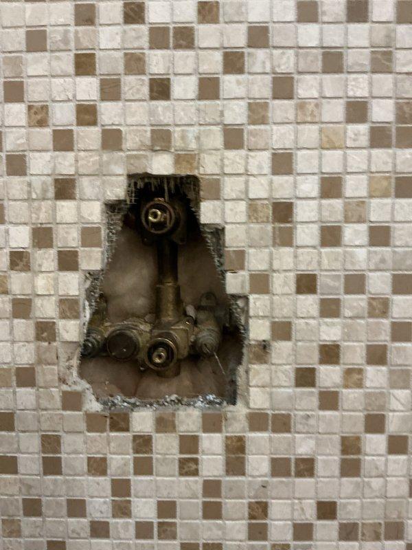 Completed shower diverter valve replacement in tiled bathroom enclosure. Accessed plumbing components through existing wall cavity containing brass valve mechanisms, removed failed diverter assembly, and installed new replacement unit. Restored proper water flow control between shower fixtures and verified operation of all valve functions.