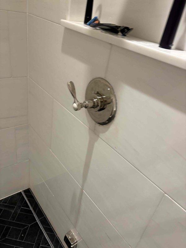 Completed shower valve replacement in residential bathroom with white subway tile surround. Removed existing chrome shower valve assembly and installed new fixture with polished chrome finish and lever handle operation. Secured valve to wall with proper escutcheon plate mounting and verified all connections for proper operation and leak-free performance.

Replaced damaged access panel lock mechanism on plumbing access point. Removed deteriorated Yale cylindrical lock assembly and surrounding compromised material. Cleaned and prepared opening, addressing water damage and paint deterioration around access panel. Installed new brass-finished cylindrical lock mechanism with proper mounting hardware to restore secure access to plumbing components behind wall cavity.
