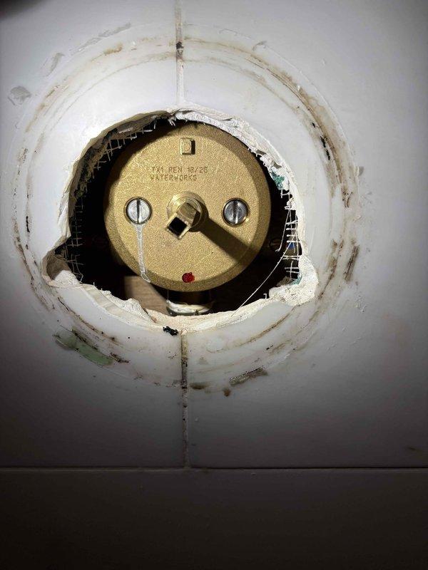 Completed shower valve replacement in residential bathroom with white subway tile surround. Removed existing chrome shower valve assembly and installed new fixture with polished chrome finish and lever handle operation. Secured valve to wall with proper escutcheon plate mounting and verified all connections for proper operation and leak-free performance.

Replaced damaged access panel lock mechanism on plumbing access point. Removed deteriorated Yale cylindrical lock assembly and surrounding compromised material. Cleaned and prepared opening, addressing water damage and paint deterioration around access panel. Installed new brass-finished cylindrical lock mechanism with proper mounting hardware to restore secure access to plumbing components behind wall cavity.