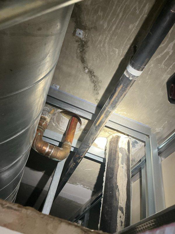 Responded to a water leak investigation in a high-rise residential unit where water was penetrating to the unit below. Upon arrival, inspected the bathroom tub area which had previously undergone drain replacement and subsequent resealing attempts. Conducted thorough visual inspection of the bathtub installation, surrounding tile work, and plumbing fixtures including chrome controls and tub spout. Examined the tub perimeter, grout lines, and caulking joints for potential breach points. Accessed the unit below to inspect ceiling penetration and plumbing infrastructure, documenting water damage patterns on concrete surfaces and identifying affected piping systems including insulated lines and copper supply lines. Photographed the bathtub installation showing corner alcove configuration with tile surround and documented the mechanical chase area below revealing pipe penetrations through ceiling structure. Investigation revealed ongoing water intrusion despite previous resealing work, indi