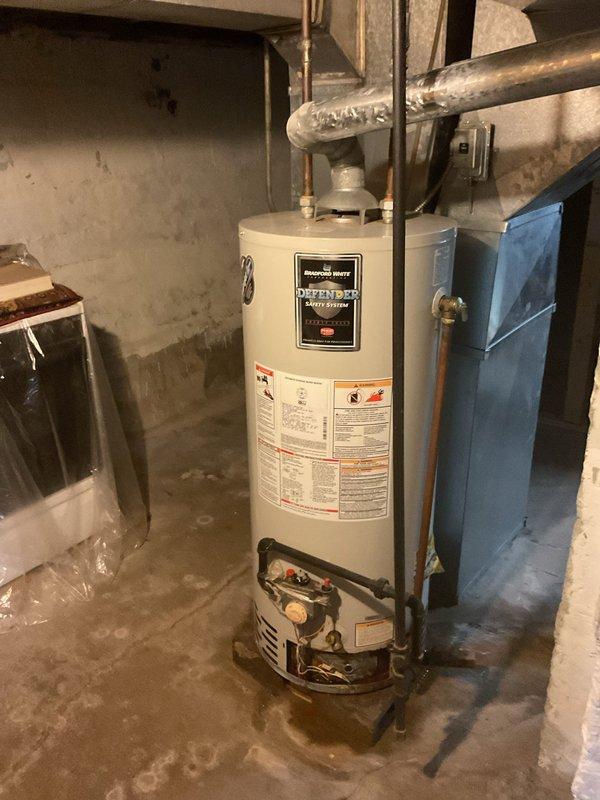 Conducted on-site assessment of existing Bradford White Defender Safety System water heater in basement utility area for replacement estimate. Evaluated current installation including copper supply line connections, shutoff valves, and plumbing configuration at top-mounted inlet/outlet ports. Inspected base connections with brass fittings and flexible connectors. Documented unit specifications, existing piping layout, and installation conditions. Noted concrete floor placement without drain pan or elevated platform. Assessed surrounding workspace access and clearances for future replacement work. Photographed equipment labels, plumbing connections, and installation environment to provide accurate replacement quotation.
