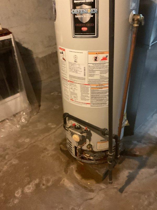 Conducted on-site assessment of existing Bradford White Defender Safety System water heater in basement utility area for replacement estimate. Evaluated current installation including copper supply line connections, shutoff valves, and plumbing configuration at top-mounted inlet/outlet ports. Inspected base connections with brass fittings and flexible connectors. Documented unit specifications, existing piping layout, and installation conditions. Noted concrete floor placement without drain pan or elevated platform. Assessed surrounding workspace access and clearances for future replacement work. Photographed equipment labels, plumbing connections, and installation environment to provide accurate replacement quotation.