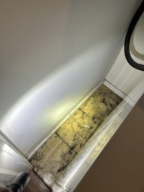 Responded to emergency service call for water leak occurring during laundry operation. Upon inspection, discovered active leak from unit causing significant water damage to flooring and baseboard area, with visible staining and deterioration present. Documented existing damage with photographic evidence showing compromised flooring material and water intrusion patterns at wall-floor junction.