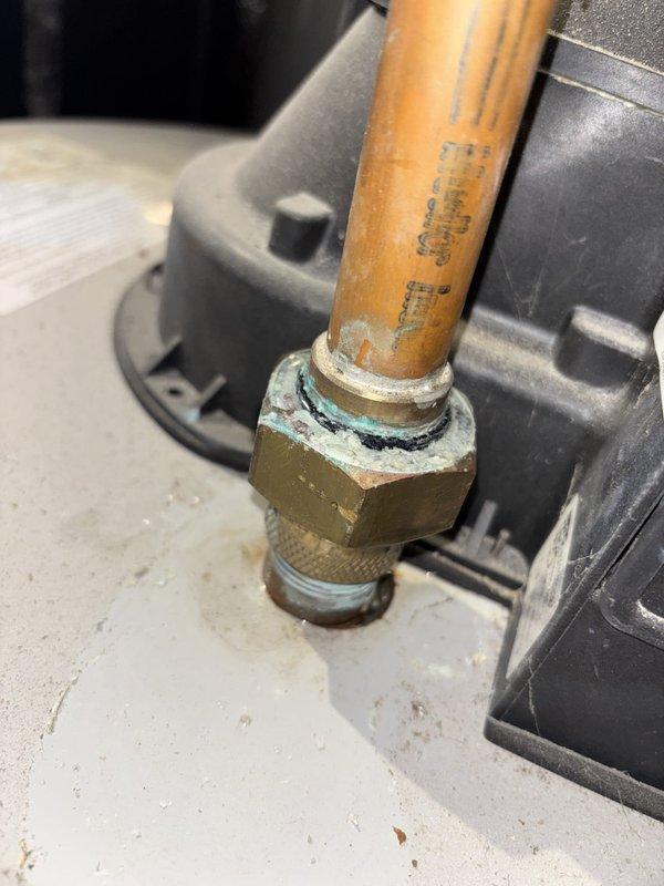 Responded to service call for tanked water heater installed in 2023 that was leaking from top connections and failing to heat water. Upon inspection, identified significant corrosion and mineral deposits on copper pipe connections and brass compression fittings at the top of the unit, with visible white-green oxidation residue indicating prolonged moisture exposure at the threaded joints. Documented the failed connections showing deteriorated gaskets and compromised seals that were allowing water to leak from the inlet/outlet plumbing connections.