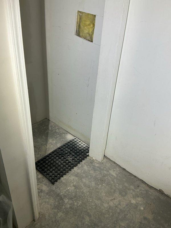 Conducted on-site drain and sewer estimate for residential property. Inspected utility closet area with concrete flooring and identified wall access panel with exposed insulation, indicating potential plumbing access point for future work. Evaluated adjacent laundry room containing washing machine and assessed drainage system accessibility for potential sewer line service or repair needs.