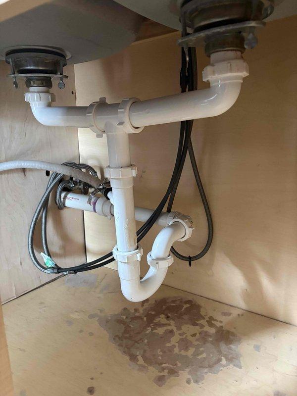 Replaced existing white PVC drain piping with copper pipe and fittings under both sinks in a double-basin kitchen sink configuration at a two-flat residence. Sourced and supplied all necessary copper pipe, fittings, and connection hardware as requested. Removed the original PVC P-trap assemblies and horizontal connector pipe linking both drain assemblies. Installed new copper piping system maintaining proper P-trap configuration for both basins. Connected new copper drain lines to existing chrome basket strainers at sink outlets and tied into main drain line. Ensured all connections were properly sealed and tested for leaks. Verified proper drainage flow from both basins upon completion. Cabinet interior showed evidence of previous water staining on floor surface, though no active leaks were present during service. All work completed within scheduled window with advance notice provided as requested.