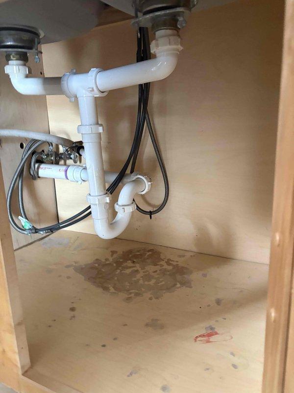 Replaced existing white PVC drain piping with copper pipe and fittings under both sinks in a double-basin kitchen sink configuration at a two-flat residence. Sourced and supplied all necessary copper pipe, fittings, and connection hardware as requested. Removed the original PVC P-trap assemblies and horizontal connector pipe linking both drain assemblies. Installed new copper piping system maintaining proper P-trap configuration for both basins. Connected new copper drain lines to existing chrome basket strainers at sink outlets and tied into main drain line. Ensured all connections were properly sealed and tested for leaks. Verified proper drainage flow from both basins upon completion. Cabinet interior showed evidence of previous water staining on floor surface, though no active leaks were present during service. All work completed within scheduled window with advance notice provided as requested.