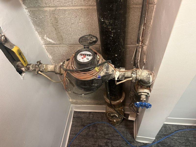 Removed existing 1.5" gate valve, nipples, and 90-degree elbow at water meter location. Installed new 1.5" female thread ball valve, 1.5" brass nipple, and 1.5" x 1" brass 90-degree elbow, utilizing existing meter nipple. Wall opening was expanded for proper access to complete valve replacement work. 

Performed video camera inspection of sewer line following reports of sewer flies at floor drain location after previous sewer pipe replacement. Televised inspection confirmed sewer line is clean with proper connections and open flow throughout. Flushed dedicated bathroom floor drain with multiple buckets of water to restore trap seal. Recommended annual sewer line inspection and regular flushing of floor drains to maintain trap seals and prevent sewer fly issues. Advised use of enzymatic drain treatment product for ongoing fly and buildup control in all drain locations.