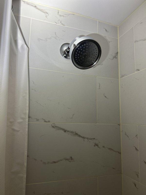 Responded to water leak complaint affecting apartment unit below. Investigated source of water intrusion emanating from bathroom exhaust fan in lower unit. Upon inspection, identified cracked vent pipe in upper unit bathroom as primary leak source. Documented conditions with photographs of shower area showing marble-pattern tile installation and plumbing fixtures, as well as laundry area where additional plumbing connections were visible. Leak location confirmed and photographic evidence provided for repair planning.
