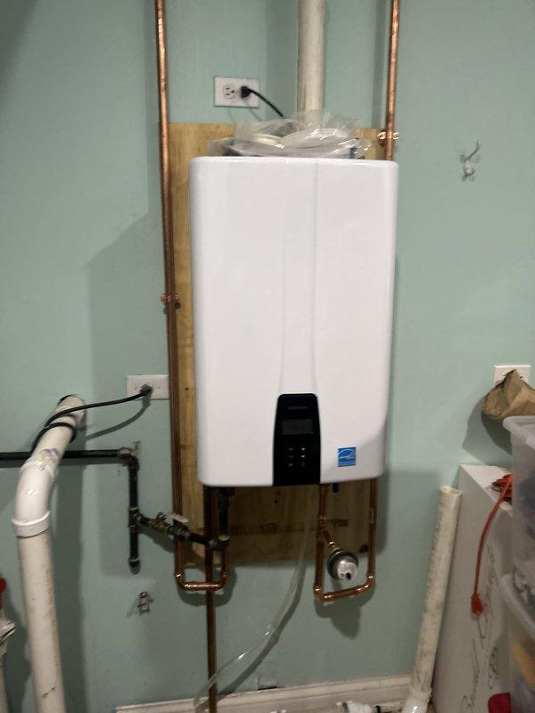 Responded to emergency service call for leaking water heater with reduced hot water capacity at residential property. Removed existing failed tanked water heater and installed new wall-mounted tankless water heater unit on backing board with proper copper supply line connections and electrical hookup. Completed initial installation including hot and cold water piping, electrical connection to dedicated outlet, and partial venting system installation. White PVC venting pipes routed through ceiling area and structural spaces. Installation requires follow-up visit to complete intake and exhaust venting penetration through foundation exterior wall. Unit temporarily operational pending final vent termination completion.