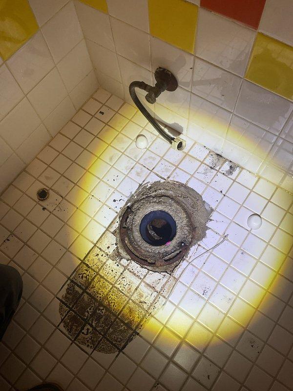 Responded to service call for toilet leak and drain backup issue. Upon arrival, discovered significant water infiltration and drainage problems in bathroom area. Inspected floor drain and toilet connection, observing discoloration and staining around fixtures indicating chronic moisture issues and potential sewage backup. Identified compromised grout lines and tile sealant allowing water penetration. Assessed flexible water supply line condition and verified proper connections. Documented existing conditions including yellowing and staining on floor tiles surrounding drain and toilet base, consistent with prolonged exposure to wastewater. Photographed affected areas showing deteriorated grout, mineral deposits, and biological staining patterns. Evaluated shower floor drain for potential cross-contamination or shared drainage concerns. Determined root cause of backup and leaking, likely due to partial blockage in main drain line or failed wax ring seal at toilet base allowing wastewater