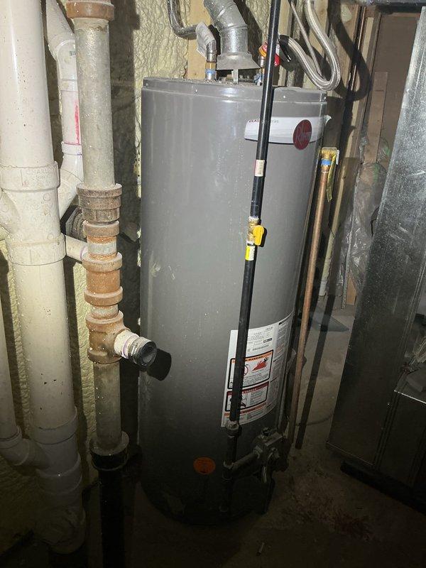 Replaced aging water heater system in basement utility area due to severe corrosion of existing metal piping and deteriorating unit condition. Removed old corroded brown metal pipes and installed new water heater with updated plumbing connections, including white PVC drainage lines and copper supply lines. Connected metallic exhaust vent ductwork to top of unit and ensured proper venting through existing infrastructure. All installations completed to current plumbing code standards with appropriate safety labeling and manufacturer specifications verified.