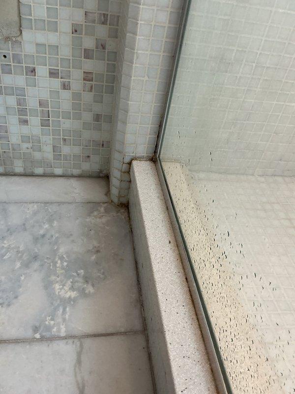 Responded to water leak investigation request from upper-unit resident after multiple lower units reported bathroom ceiling leaks. Conducted thorough inspection of bathroom plumbing fixtures and surrounding areas to determine if unit was the source of water intrusion. Visual examination revealed significant deterioration of toilet flange seal with heavy rust corrosion and staining on surrounding floor tiles, indicating potential leak point. Shower enclosure corner showed moisture-related discoloration, rust staining on metal door track components, and water spotting on wall tiles. Documented all findings with photographs showing compromised toilet seal with rust-colored gasket deterioration and mineral deposits radiating from drain area, as well as corner moisture damage and oxidation of shower door hardware. Provided photographic evidence to confirm presence of potential leak sources requiring repair to prevent continued water damage to units below.