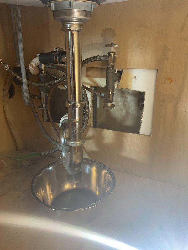 Responded to water leak under kitchen sink. Upon inspection, identified leaking P-trap assembly with visible corrosion and compromised seal connections. Disassembled chrome-plated P-trap, cleaned all connection points, and replaced worn washers and slip joint gaskets. Reassembled drain assembly with proper alignment and torque specifications. Tested system under full water flow to verify leak resolution and proper drainage. Cabinet interior showed minor water staining on wall panel, indicating previous moisture exposure now resolved.