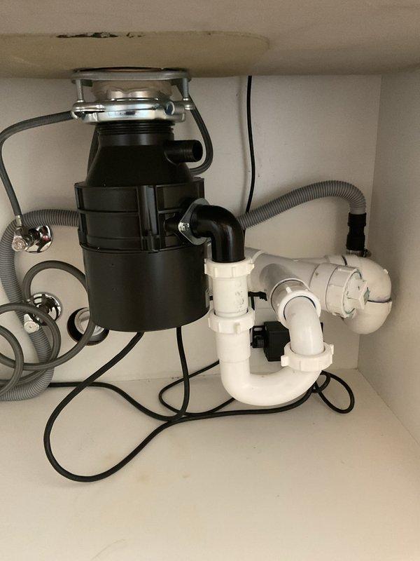 Responded to service call for garbage disposal repair. Upon arrival, performed comprehensive inspection of the disposal unit and associated plumbing assembly beneath the kitchen sink. Evaluated the black garbage disposal unit, mounting assembly, and all connected components including the P-trap configuration, drainage hoses, and electrical connections. Verified proper operation of the disposal unit and tested all plumbing connections for leaks. Inspected the sink flange mounting, discharge connections, and dishwasher drain line attachment points. Ensured all white PVC piping, elbow fittings, and trap assembly were properly secured and functioning correctly. Confirmed electrical connections were safe and operational. All components found to be in working order upon completion of inspection and testing.