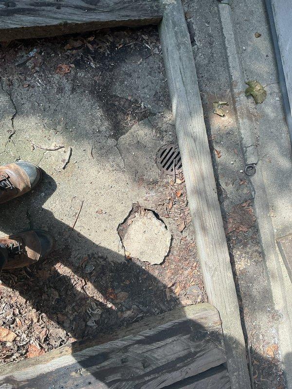 Responded to site visit for plumbing assessment of outdoor drainage and underground piping system. Upon arrival, accessed property using entry code provided by customer. Conducted thorough inspection of exterior concrete surface area, documenting significant deterioration including large circular crack pattern with exposed aggregate and multiple areas of concrete separation. Noted functional floor drain present in outdoor surface area with visible grid grate.

Proceeded to interior workspace where active plumbing installation was in progress. Inspected white PVC drainage piping sections approximately 3-4 inches in diameter with standard coupling fittings positioned on concrete floor. Documented construction materials on-site including bags of sand/cement mix stored on shelving and loose fill material staged for installation work. Verified plumbing components and materials were appropriate for scope of work.

Comprehensive photographic documentation captured for service records showing 