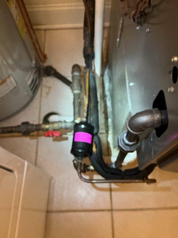 Responded to water leak investigation in laundry room area where customer reported slow leak appearing around ceiling light fixture, suspected to originate from unit above. Performed visual inspection of affected ceiling area, documenting extensive water staining and discoloration on textured ceiling surface near plumbing penetrations and vent opening. Examined exposed piping infrastructure including copper lines, PVC components, and metal fixtures in utility space to identify potential leak source. Based on staining patterns and pipe locations, determined leak likely originates from plumbing system in upper unit requiring coordination with above-unit access for definitive source identification and repair.