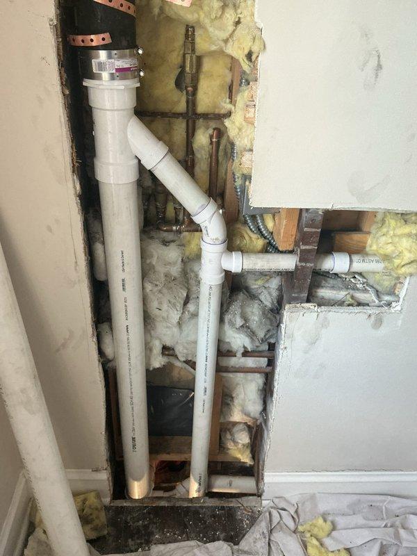 Completed plumbing repair involving replacement of drainage and vent piping within an interior wall cavity. Opened wall to access existing copper plumbing infrastructure, installed new white PVC drain and vent lines, and secured all piping to wall studs with appropriate metal strapping. Protected surrounding areas with drop cloths and plastic sheeting throughout the work area to maintain cleanliness during the repair process.