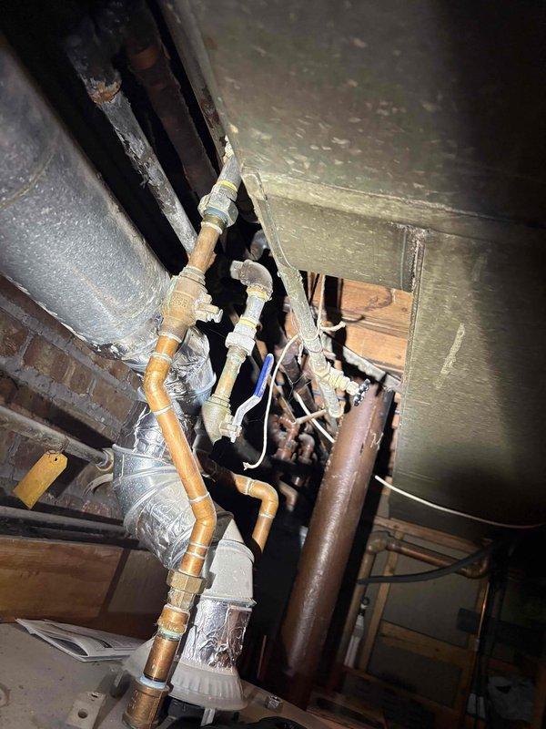 Completed comprehensive plumbing estimate for piping system replacement in utility area featuring deteriorated copper supply lines with extensive corrosion and mineral deposit buildup, aging PVC drain and waste lines with visible purple primer at connections, and compromised infrastructure along exposed brick foundation wall. Documented existing conditions including corroded brass fittings, valves requiring replacement, and multiple pipe runs servicing the mechanical systems in preparation for complete repiping specifications.