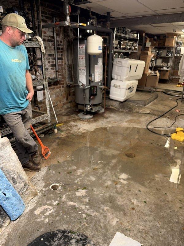 Responded to a commercial property experiencing significant water accumulation in the basement utility area. Upon arrival, observed extensive standing water and pooling throughout the concrete floor surrounding the water heater and electrical infrastructure. Conducted thorough assessment of the drainage system to identify the source of flooding and potential blockages in the floor drain system. Inspected the circular floor drain access point and surrounding plumbing connections to determine the cause of water backup. Evaluated the condition of the sewer and drainage lines servicing the basement level and provided comprehensive estimate for necessary drain cleaning, potential line repairs, and water extraction services to restore proper drainage function and prevent future flooding incidents.