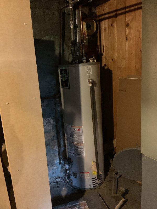 Completed water heater installation in basement utility area. Installed new white cylindrical water heater with proper plumbing connections, including black metal pipe fittings and pressure relief valve assembly at top of unit. Connected copper supply lines and verified all connections secure. Installed wall-mounted electronic control panel for system operation. Tested unit for proper functionality and confirmed no leaks at connections. System operational and ready for use.