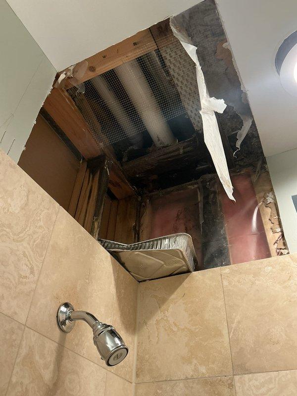 Responded to water leak investigation between two bathrooms where drywall had been previously opened by occupant. Located active drip originating from plumbing pipe in ceiling cavity above lower bathroom, with water traveling through to adjacent bathroom space. Documented existing ceiling damage, exposed framing, and temporary catch pan placement. Confirmed leak source and provided findings for repair recommendations.