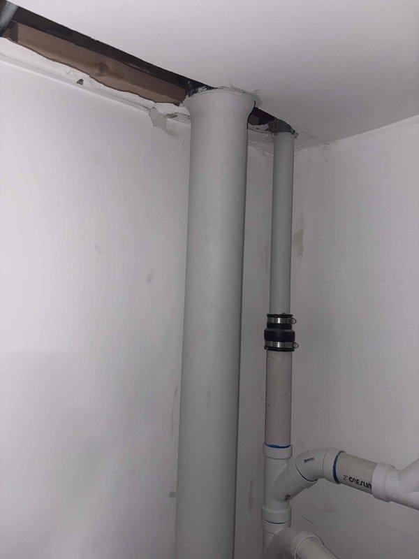 Conducted comprehensive plumbing assessment of residential property to evaluate aging galvanized piping system experiencing ongoing operational issues. Inspected vertical pipe runs with insulated gray foam wrapping extending floor to ceiling, documented existing PVC connections with elbow joint configurations, and examined ceiling access point revealing structural components where piping penetrates through drywall. Evaluated bathroom plumbing infrastructure including chrome fixture installations, tub spout assembly, and shower arm connections mounted to black marble tile surround to determine scope of galvanized pipe replacement required throughout the home.