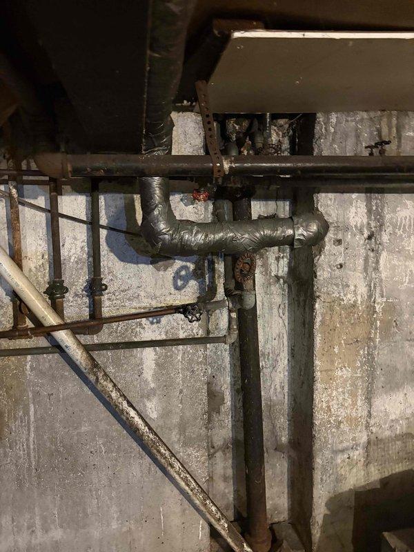 Conducted comprehensive plumbing assessment of aging basement mechanical infrastructure, documenting extensive deterioration of existing piping system including corroded metal components, compromised pipe joints, and weathered fixtures. Photographed moisture-damaged concrete block walls exhibiting efflorescence and mold growth, along with multiple horizontal and vertical pipe runs showing significant corrosion requiring replacement or repair recommendations for copper, galvanized, and flexible ductwork connections.