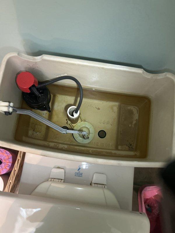 Responded to non-emergency plumbing service call to assess multiple plumbing concerns. Inspected toilet tank interior and identified significant hard water mineral deposits, sediment accumulation, and discolored water within the Crane Plumbing toilet tank. Documented condition of flush valve assembly, fill valve with float mechanism, and flapper chain system, all showing signs of age-related wear and mineral buildup on porcelain surfaces.
