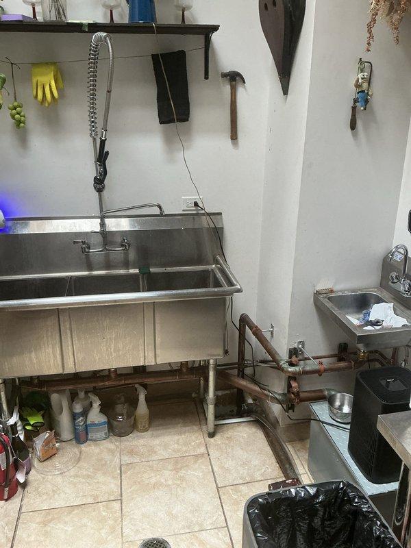 Conducted site assessment for grease trap installation in commercial kitchen area. Evaluated existing three-compartment stainless steel sink configuration and current drainage system. Inspected basement plumbing infrastructure including overhead drain lines and floor access points. Provided estimate for concrete floor removal and installation of new drain connection to properly integrate grease trap into existing wastewater system.