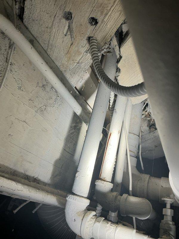 Responded to report of small water leak in basement. Conducted thorough visual inspection of exposed plumbing infrastructure including PVC drain lines, copper supply lines, and associated HVAC ductwork mounted to ceiling joists. Examined all visible pipe joints, connections, and mounting brackets for signs of active leakage, moisture accumulation, or water damage. Documented existing plumbing configuration with photographs showing white PVC drainage system, copper water supply piping, and flexible corrugated ventilation ducting. Inspected ceiling surfaces for water staining, discoloration, or structural compromise that would indicate leak source location. Assessed condition of pipe supports and hangers to ensure proper drainage slope and system integrity. Leak location investigation completed with photographic documentation provided for record and future reference.