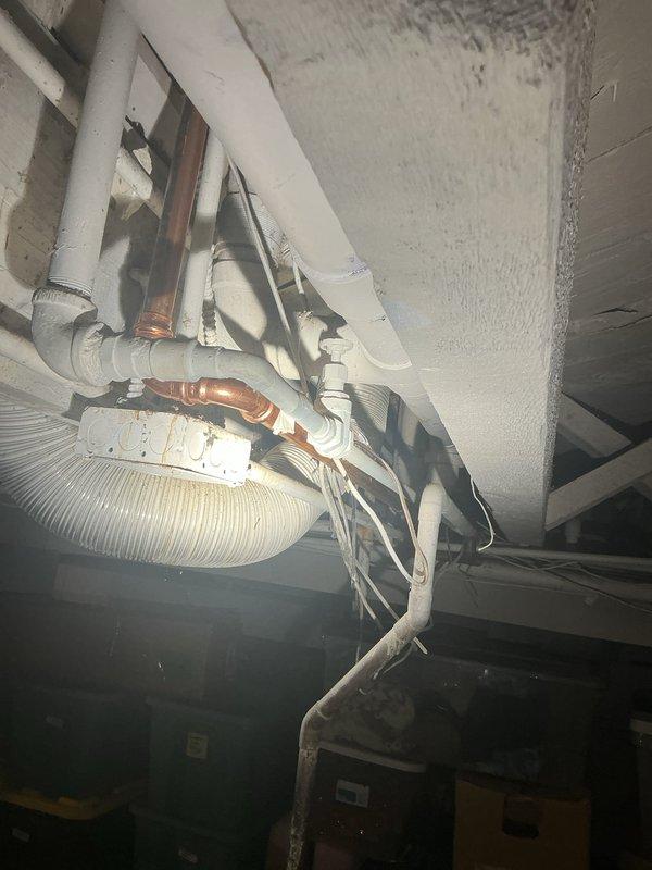 Responded to report of small water leak in basement. Conducted thorough visual inspection of exposed plumbing infrastructure including PVC drain lines, copper supply lines, and associated HVAC ductwork mounted to ceiling joists. Examined all visible pipe joints, connections, and mounting brackets for signs of active leakage, moisture accumulation, or water damage. Documented existing plumbing configuration with photographs showing white PVC drainage system, copper water supply piping, and flexible corrugated ventilation ducting. Inspected ceiling surfaces for water staining, discoloration, or structural compromise that would indicate leak source location. Assessed condition of pipe supports and hangers to ensure proper drainage slope and system integrity. Leak location investigation completed with photographic documentation provided for record and future reference.